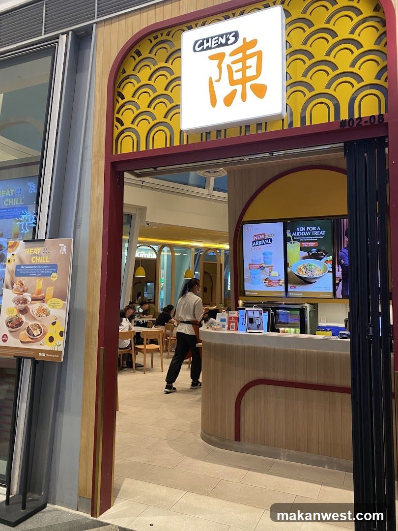 The exterior of a restaurant called Chen's, with a prominent sign featuring Chinese characters. The entrance is arched and decorated with yellow wave-like patterns. Inside, customers are seated at tables, and a staff member is visible behind the counter. Digital screens display menu items and promotions.