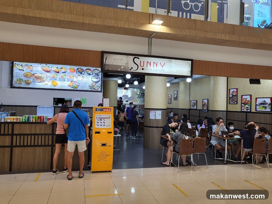 A food stall with a large menu board displaying various Korean dishes. People are seen ordering and dining at tables.