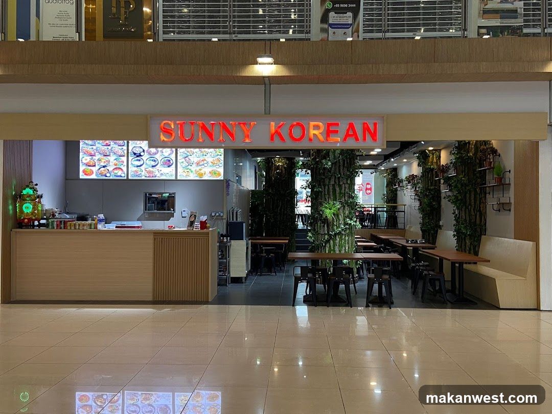 A storefront with a bright red neon sign that reads "SUNNY KOREAN". In front of the counter, there are three illuminated menu boards displaying various Korean dishes with pictures. The interior features tables and chairs, with decorative artificial trees and plants creating a unique ambiance. A long, light-colored banquette seating is visible on the right side.