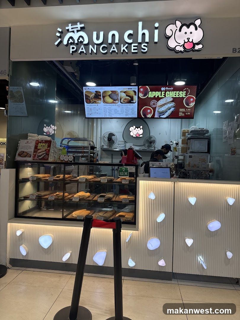 A storefront for Munchi Pancakes, featuring a display case filled with various pancakes and a menu board above. The shop has a modern design with illuminated decorative elements on the counter.