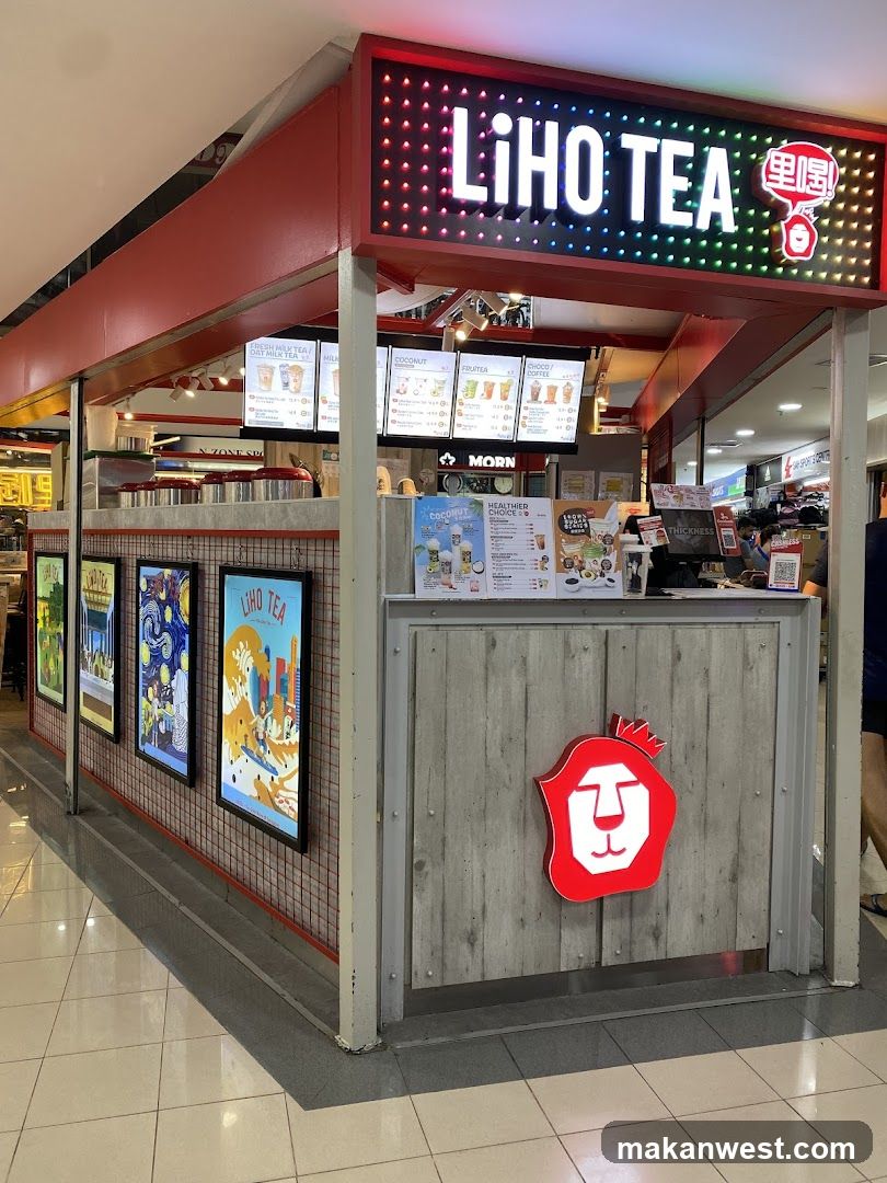 A LiHo Tea shop front with a prominent red and white lion logo. The shop has a bright LED sign displaying "LiHO TEA" and Chinese characters. There are framed posters on the left side of the shop and menu boards above the counter.