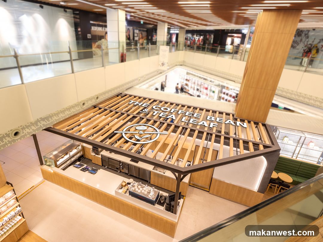 A coffee and tea shop with a modern wooden exterior and interior, located within a shopping mall. The shop features a counter with espresso machines, display cases, and seating areas.