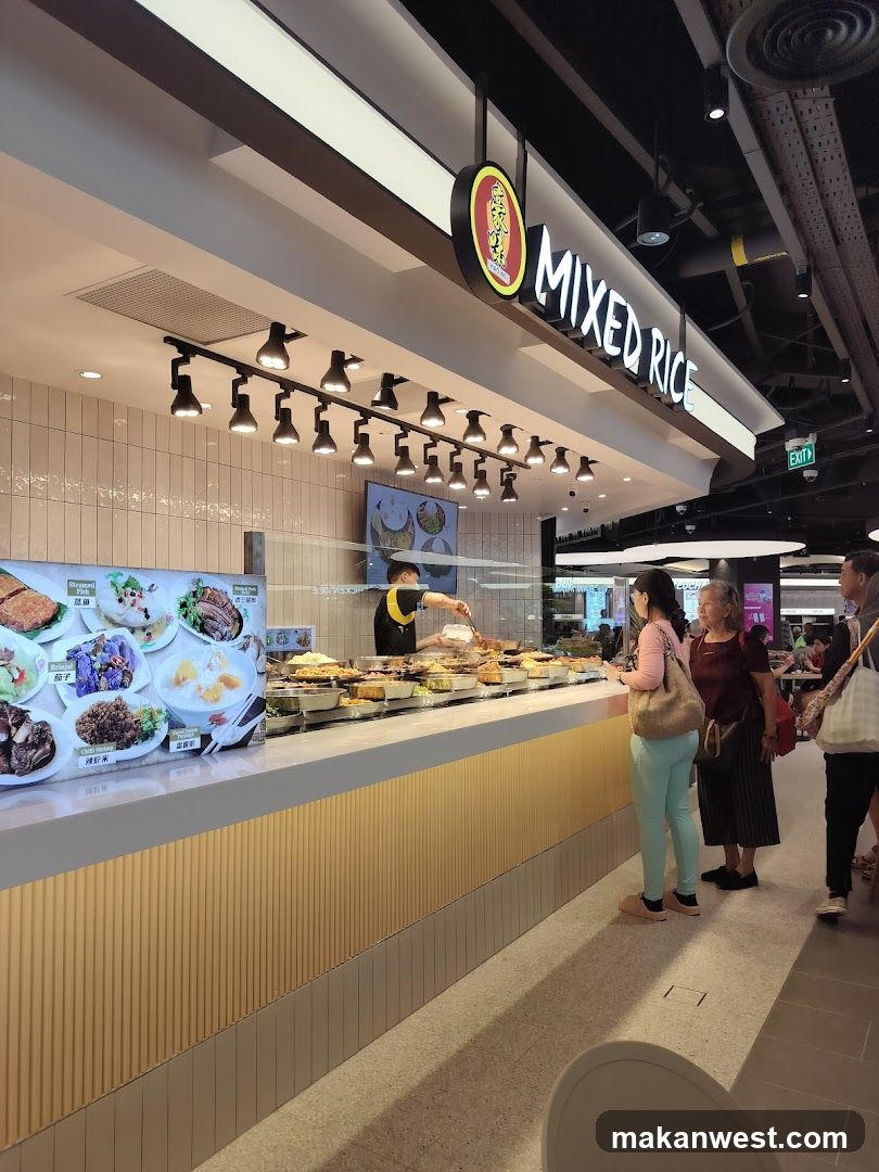A food stall with a sign that reads "MIXED RICE". A server is dishing out food to customers. There are many dishes displayed behind a glass counter. A menu board with pictures of food items is visible on the left.