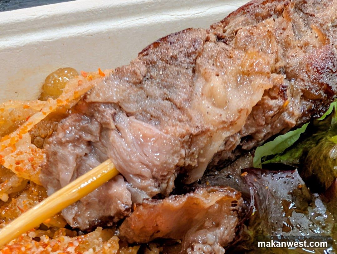 Close-up of a skewer of meat with crispy bits and greens