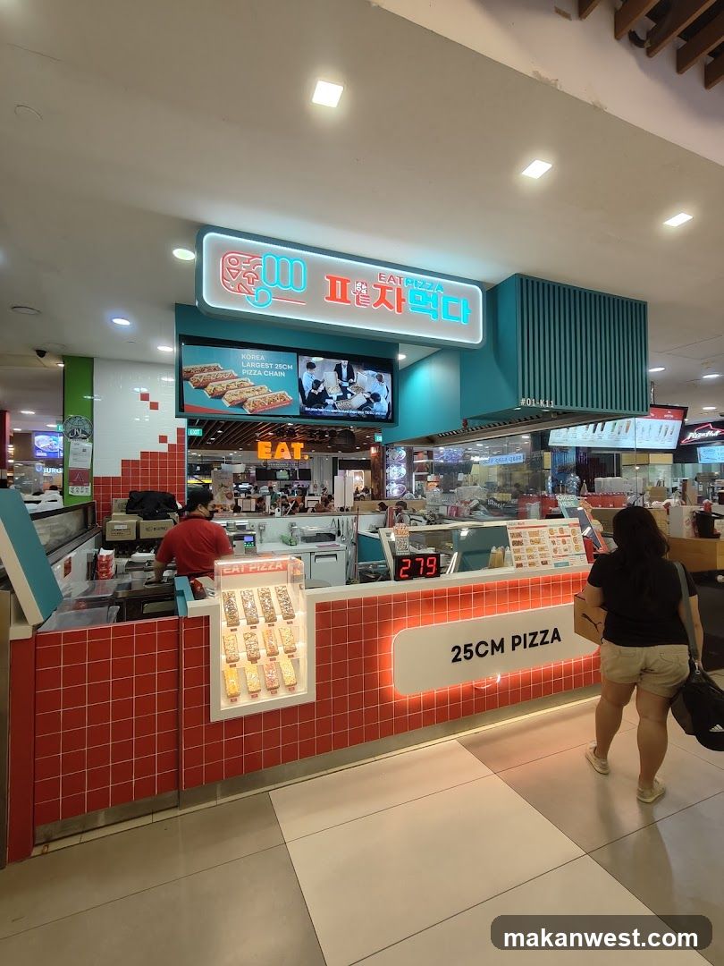 A brightly lit pizza shop with a red tiled counter and a prominent neon sign that reads "EAT PIZZA" in English and Korean. A digital display shows "279". A screen above the counter shows images of pizzas and people. A sign on the counter advertises "25CM PIZZA".
