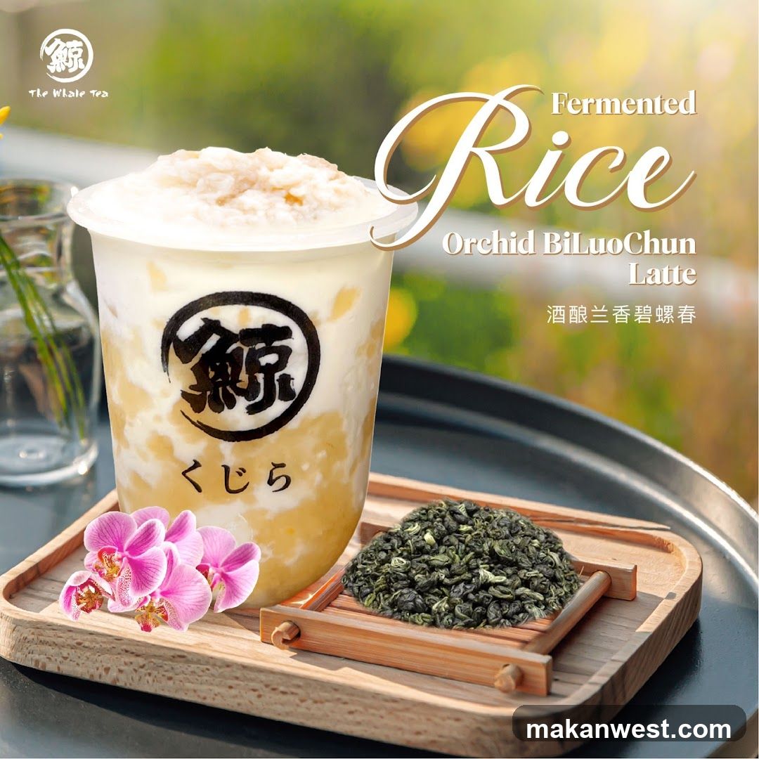 A close-up of a drink with a creamy white top and yellow layers inside a clear plastic cup. The cup has a black logo with Japanese characters and the text "The Whale Tea" below it. In front of the cup, on a wooden tray, are pink orchids and a small pile of green tea leaves. The background is blurred green foliage.