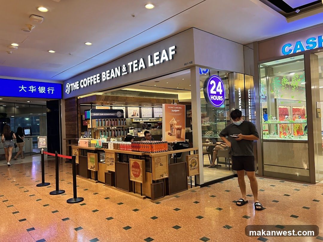 The exterior of The Coffee Bean & Tea Leaf shop, with its prominent signage. The shop is open 24 hours and displays various merchandise and promotional materials. A person is standing outside the shop looking at their phone.
