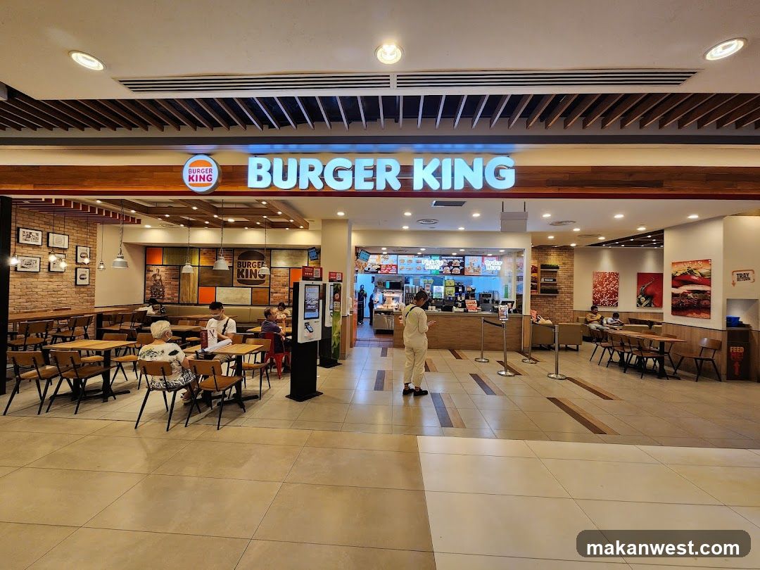The exterior of a Burger King restaurant with its prominent signage. Inside, tables and chairs are visible, with some customers seated. The ordering counter and menu boards are also visible.