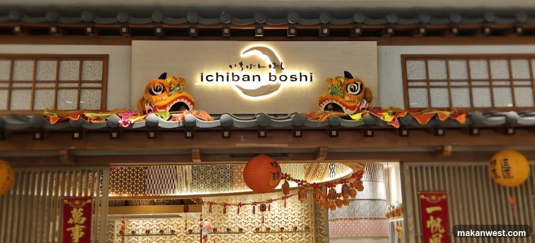 The exterior of a Japanese restaurant with traditional architectural elements. A prominent illuminated sign reads "ichiban boshi" with a crescent moon logo. Two decorative lion heads are placed on the roofline, adorned with colorful fabric. Red lanterns and banners with Chinese characters hang near the entrance, suggesting a festive occasion. The entrance features patterned screens and decorative lighting.