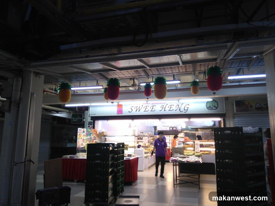 The exterior of a bakery with a prominent sign that reads "SWEE HENG". The shop front features display cases filled with baked goods and a few staff members visible inside. Pineapple-shaped lanterns are hanging from the ceiling.