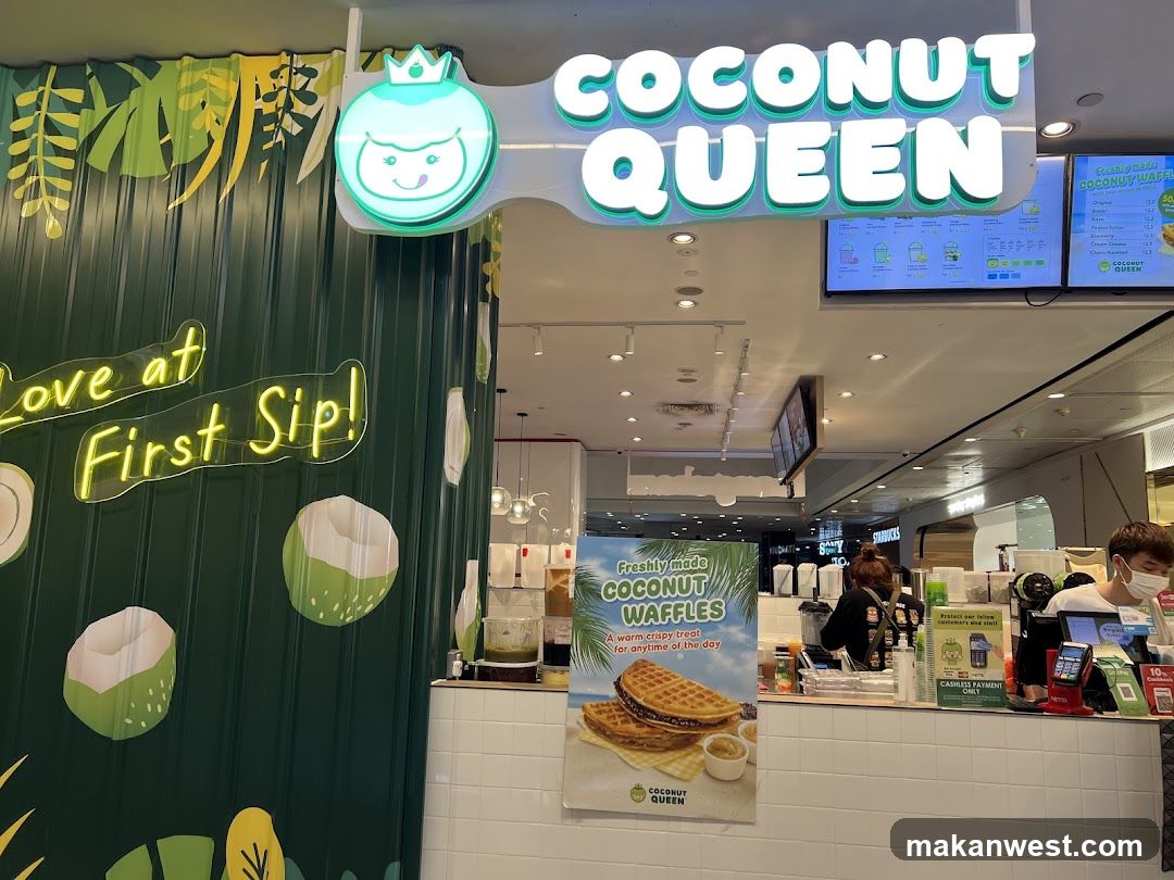 A brightly lit storefront with the "Coconut Queen" logo and name prominently displayed. The facade features green corrugated metal walls decorated with tropical leaf motifs and neon signs that say "Love at First Sip!". A large poster showcases freshly made coconut waffles. Inside, staff members are visible behind the counter, and digital menu boards are mounted on the ceiling.