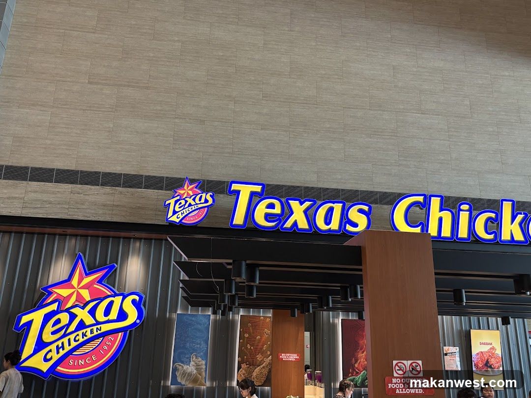 Photo of physical exterior entrance/storefront facade with visible signage ON the building. Large illuminated 'Texas Chicken' sign above entrance, logo on left wall, and vertical banners inside. No menu boards or price lists visible.