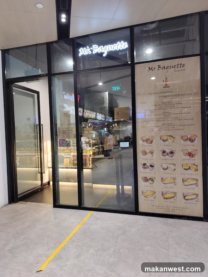 A modern glass-fronted bakery with illuminated signage reading 'Mr Baguette' above the entrance. A large menu board is mounted on the right side of the facade, displaying various bread and pastry items with prices. The interior shows display cases filled with baked goods.