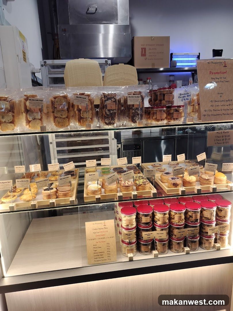 A glass display case in a bakery or cafe, showcasing various baked goods including breads, pastries, and jars of cookies. A menu board is visible on the right side of the counter.