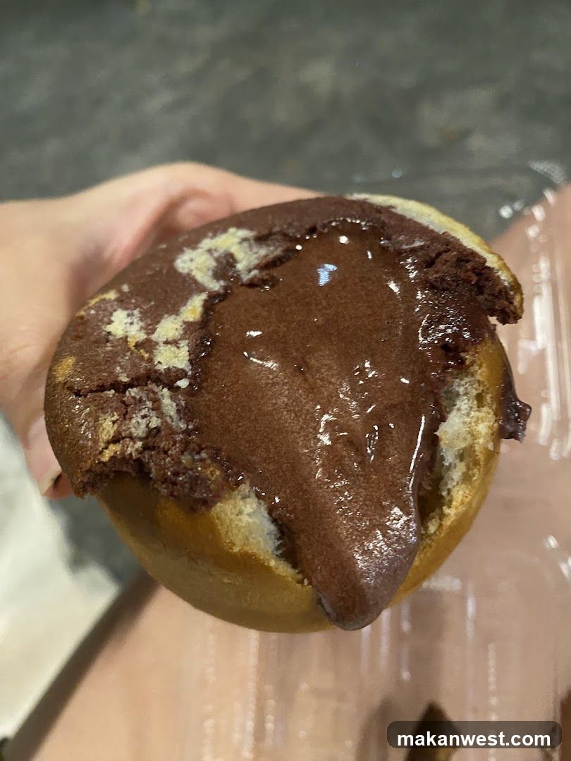 A hand holds a partially eaten donut with rich chocolate filling oozing out, showing visible crumbs and glossy texture.