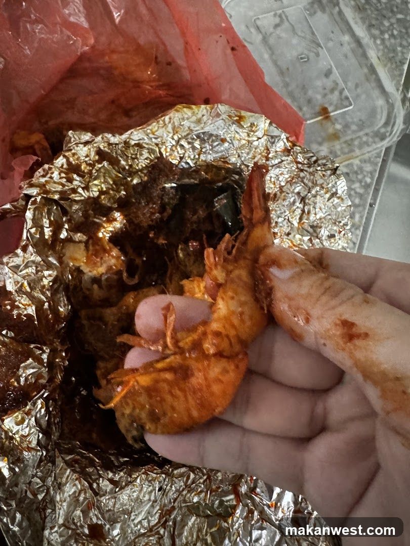 Hand holding spicy shrimp with foil-wrapped food