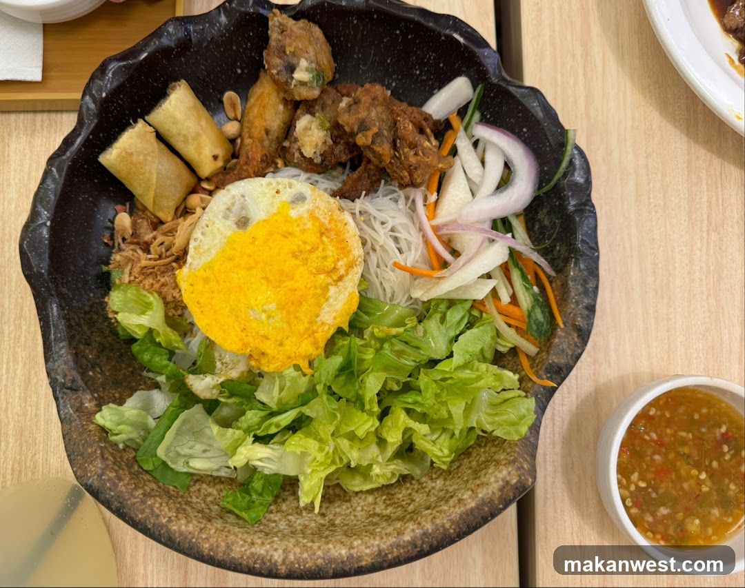 Bowl of Vietnamese-style noodle dish with fried egg and spring rolls