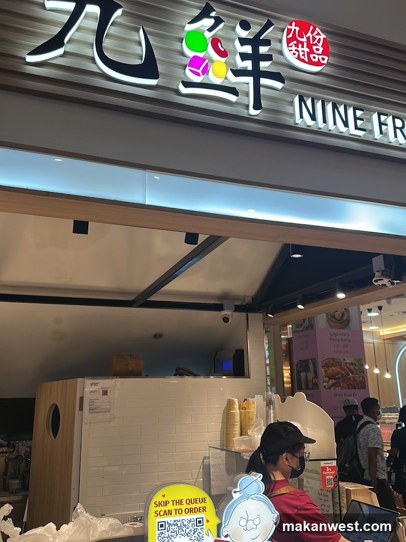 The image shows the storefront of a dessert shop named 'Nine Fresh' (九鲜甜品). The sign features large Chinese characters with colorful macaron illustrations and English text 'NINE FR'. Below, there is a counter area with stacked cups, a QR code standee saying 'SKIP THE QUEUE SCAN TO ORDER', and staff wearing masks. A poster on the right advertises 'Legendary Hong Kong style desserts'.