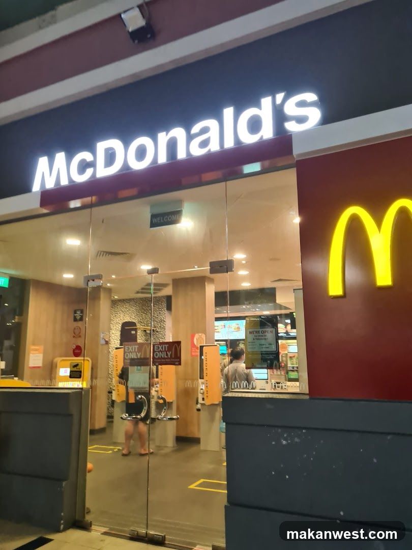 Photo of the physical exterior entrance of a McDonald's restaurant, showing illuminated signage with 'McDonald's' and the golden arches logo on the building facade.