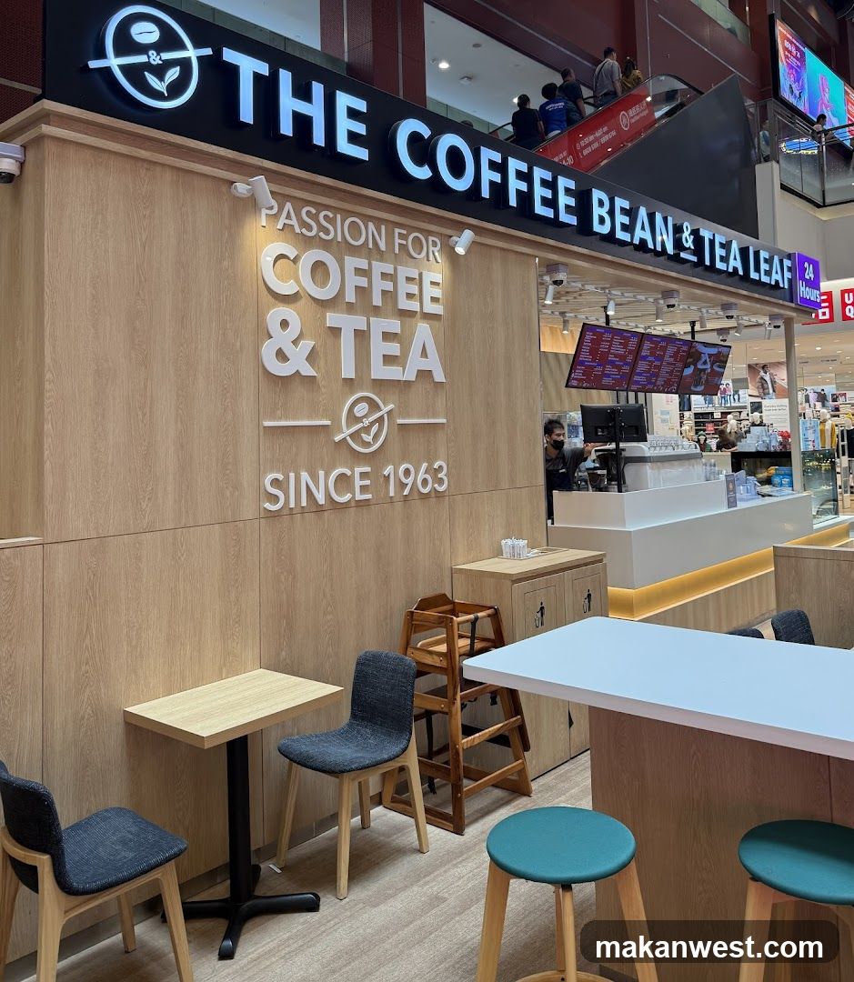 A modern coffee shop exterior with wooden paneling and illuminated signage reading 'THE COFFEE BEAN & TEA LEAF' above the entrance. The wall features a vertical sign stating 'PASSION FOR COFFEE & TEA SINCE 1963'. Inside, a white counter is visible with menu boards displaying various drink options on digital screens. Seating includes small tables with gray chairs and teal stools near the counter.