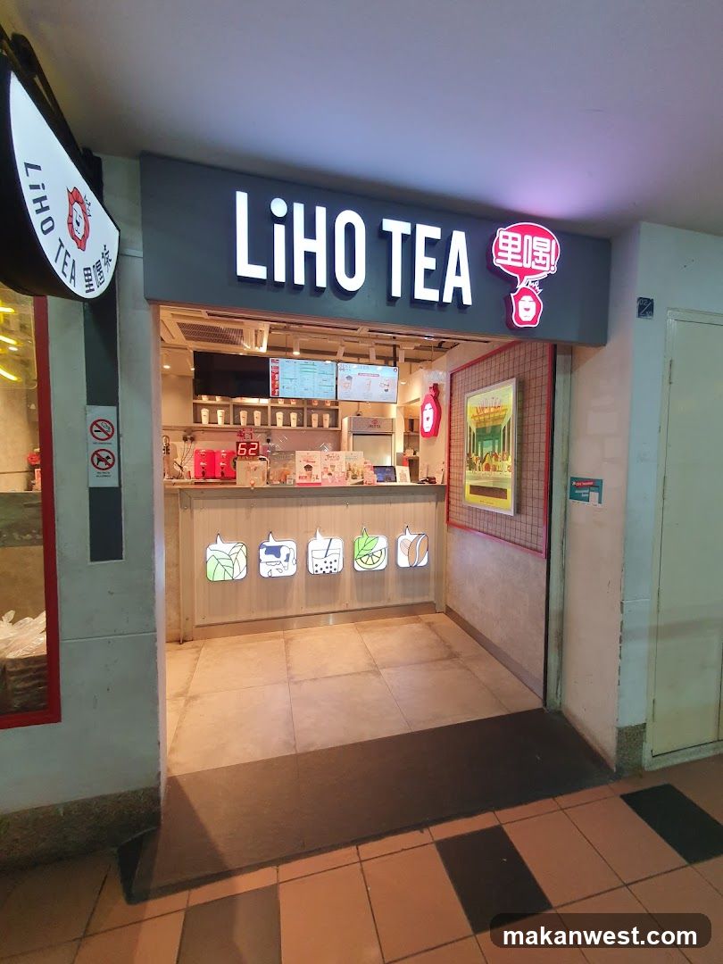 The image shows the exterior entrance of a LiHO TEA shop, featuring a prominent sign with illuminated lettering and Chinese characters. The counter is visible inside, displaying various drink options through backlit icons on the front panel.