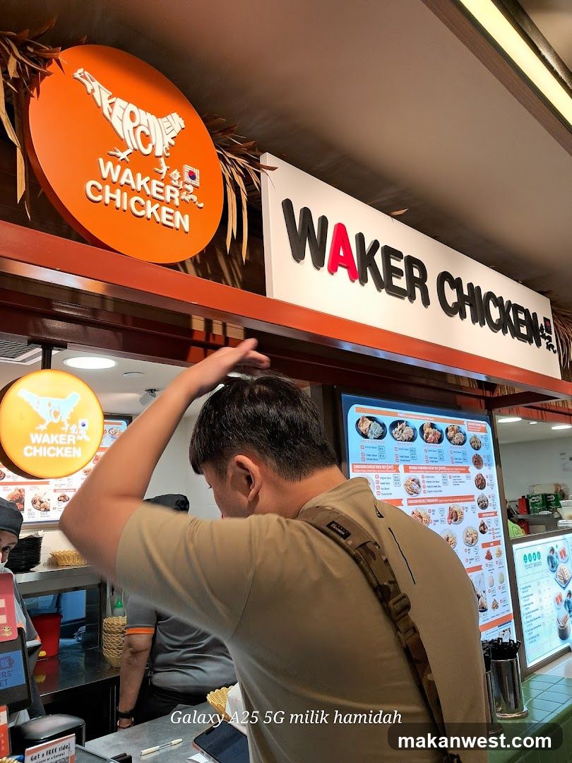 A food stall with orange and white signage displaying 'WAKER CHICKEN' in bold letters. A circular logo featuring a chicken silhouette is visible above the entrance. Inside, menu boards show various dishes with prices. A customer stands at the counter, interacting with staff.