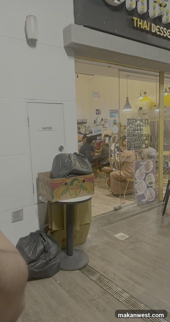 A storefront with a glass entrance showing customers inside. A sign above reads 'THAI DESERT'. Outside, there are trash bags and boxes near the wall.