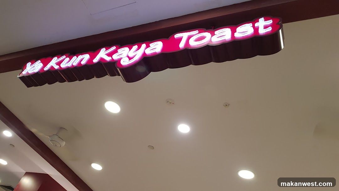 A close-up view of the illuminated sign above a shop entrance, displaying 'Yeo Kun Kaya Toast' in white lettering on a pink background with red trim.