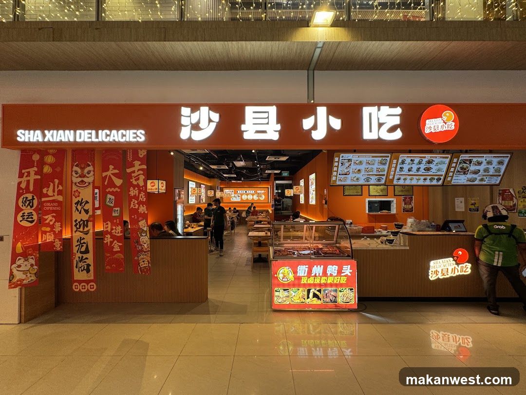 A brightly lit storefront of a Shaanxi Delicacies restaurant, featuring an orange facade with illuminated Chinese characters and English signage. Red festive banners hang on the left side. Inside, customers are seated at tables under warm lighting. A digital menu board is visible above the counter. A promotional standee in front advertises local specialties like duck necks.