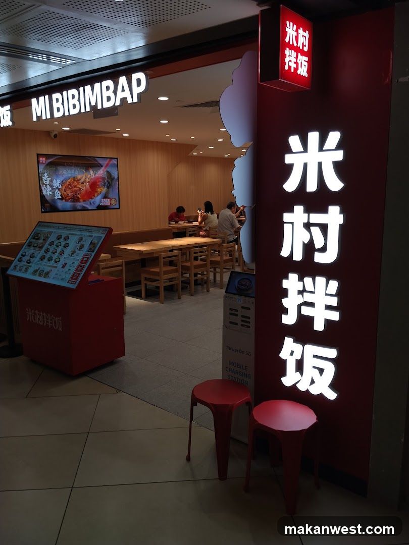 The image shows the exterior entrance of a Mi Bibimbap restaurant, featuring prominent signage with 'MI BIBIMBAP' in English and Chinese characters '米村拌饭'. Inside, customers are seated at wooden tables, and a digital menu board is visible on the left side.