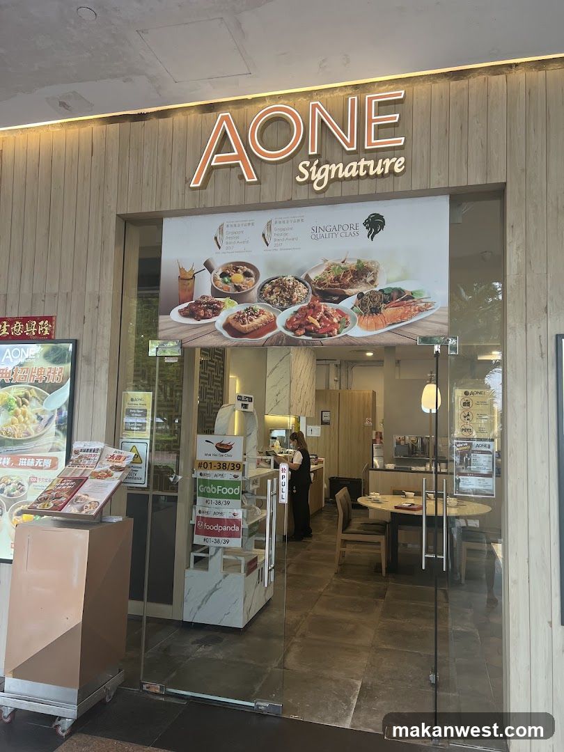 The image shows the storefront of AONE Signature, a restaurant with wooden paneling and glass doors. Inside, there are tables and chairs visible. Outside, there is a menu stand displaying various food items.
